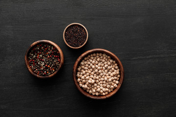 Obraz na płótnie Canvas top view on brown bowls with peppercorns, black quinoa and chickpea on dark wooden surface