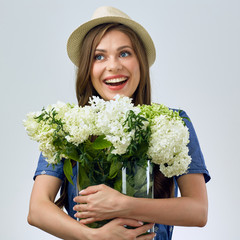 smiling woman holding white and green flowers in big glass vase.