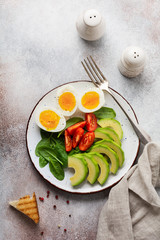 Healthy vegetarian salad breakfast. Spinach leaves, tomato, avocado and boiled egg on gray plate and gray concrete old background. Buddha bowl. Top view.