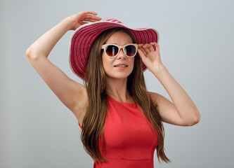 Smiling woman in summer red dress and big hat touching her sunglasses.