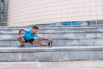 Male athlete, gymnastics stretching muscles legs before jogging. In summer spring city. Active lifestyle, workout, fitness fresh air. Motivation for sports. T-shirt shorts sneakers. Free space text.