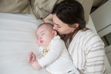 Fototapeta na wymiar happy young mother kissing her newborn baby sleep in bed. lifestyle mother's day concept
