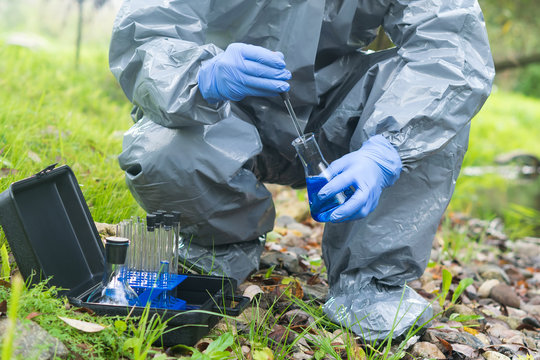 a specialist in a protective suit and blue rubber gloves in nature does a water analysis using a flask with a blue reagent and a pipette, close-up