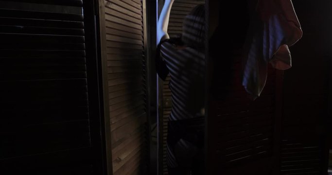 Sexy woman puts on her bra behind wooden folding screen.