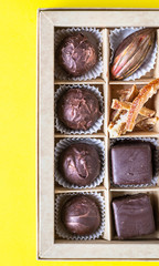 Assortment of sweet confectionery with chocolate candies and pralines in a gift box on a yellow paper background. Top view. 