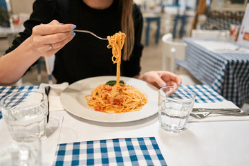 Close-up spaghetti Bolognese wind it around a fork. Parmesan cheese. Young woman eats Italian pasta with tomato, meat.