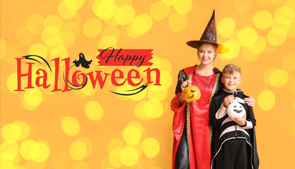Mother with little son in Halloween costumes and with pumpkins on color background