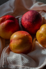 Nectarines with water droplets on a pink tea towel.  Sunlight casting shadows on the fruit