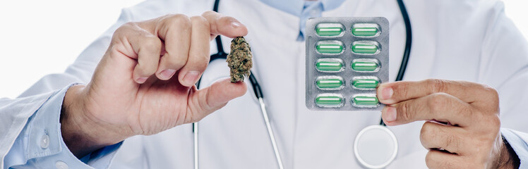 panoramic shot of doctor in white coat holding medical cannabis and pills isolated on white