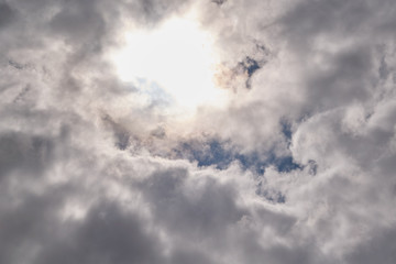 Cumulus clouds thicken toward the center. The sun is shining behind the clouds. A bright spot of sunlight is scattered by clouds. The blue sky is overcast with rain clouds. Background or backdrop.