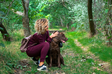 Naklejka na ściany i meble blonde curly girl plays with chocolate labrador in the autumn park on the green alley