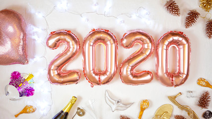 Happy New Year's Eve 2020 rose gold metallic balloons on white background with party decorations and fairy lights.