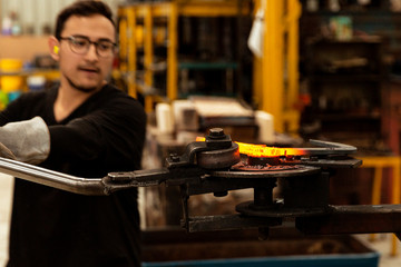 Young blacksmith working hard on manually bending steel bar into place.