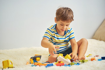 happy asian boy playing with colorful construction plastic blocks on white Bed at home.