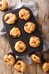 Snack savory muffins with sun-dried tomatoes and cheddar cheese close-up in a baking dish. Vertical top view