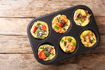 Frittata in the form of egg muffins with vegetables, cheese, bacon and mushrooms close-up in a baking dish. Horizontal top view