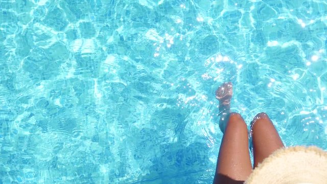 Girl in bikini relaxing in swimming pool in sunny day. Beautiful sexy girl in summer pool splashing water with feet. Top view of female beautiful legs in water. 4K