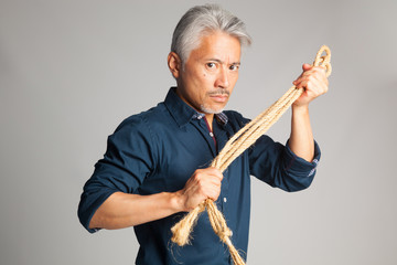 Hombre de mediana edad de origen japonés con una cuerda en sus manos y mirada amenazadora y muy...