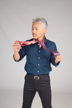 Hombre de mediana edad de origen japon&eacute;s, seleccionando una corbata, dudando que corbata ponerse