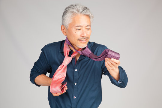 Hombre de mediana edad de origen japon&eacute;s, seleccionando una corbata, dudando que corbata ponerse