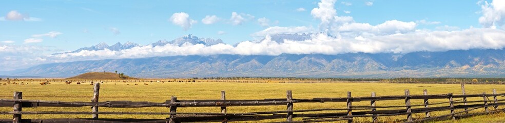 Panoramic view of the endless fields and pastures of the foothill Tunka Valley and in the distance the mountain range of the East Sayan with low clouds on a sunny autumn day