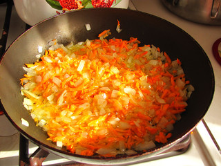 Onions and carrots are fried in a pan on the stove. Close view.