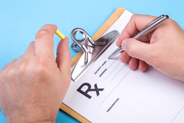 Male doctor or pharmacist holding jar or bottle of pills in hand and writing prescription on a special form. medical costs and healthcare payment concept.