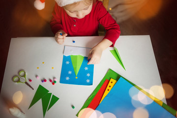 a little girl makes a card application of colored paper with the Christmas tree. the concept of winter kids creativity