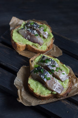 Sandwiches with avocado and herring sprinkled with raw onion on grain bread is a top view of a paper towel and stand on a dark wooden background top view