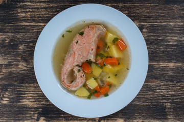 Fresh salmon fish soup with carrots and potatoes in a white plate, close up