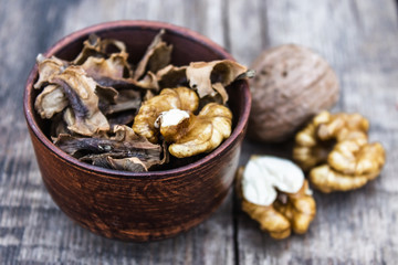 Walnut kernels and partitions in a bowl and whole walnuts on a wooden table. A medicine for tinctures and decoctions.