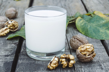 Vegan nut milk in a glass near walnuts on an old wooden table. Vegan milk from walnuts. Eco food.