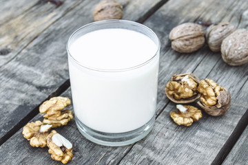 Vegan nut milk in a glass near walnuts on an old wooden table. Vegan milk from walnuts. Eco food.