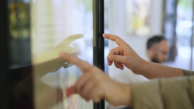 Woman using touchscreen terminal in mall. Detail view outstretched female hand touching modern big timetable or info screen in interior. Side view fingers swiping on display at out of focus background