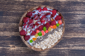 Smoothie in coconut bowl with raspberries, oatmeal, candied fruit and chia seeds for breakfast , close up. The concept of healthy eating, superfood