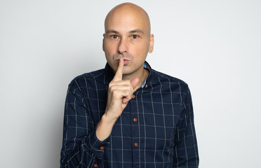 40 years old bald man is holding index finger on lips