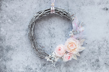 Beautiful handmade wreath made of natural birch branches and decorated with pper roses and shiny glitter balls against grey concrete background. Winter holiday or Christmas greeting