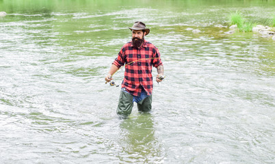 Man bearded fisher. Fishing requires to be mindful and fully present in moment. Fisher fishing equipment. Rest and recreation. Fisher masculine hobby. Fish on hook. Brutal man stand in river water