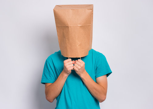Portrait of teen boy with paper bag over head. Teenager cover head with bag holding hand near face posing in studio. Child pulling paper bag over head.