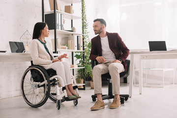 disabled businesswoman in wheelchair gesturing while talking to business partner in office