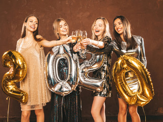 Fototapeta na wymiar Beautiful Women Celebrating New Year.Happy Gorgeous Girls In Stylish Sexy Party Dresses Holding Gold and Silver 2020 Balloons, Having Fun At New Year's Eve Party.Сarrying and drinking champagne flutes