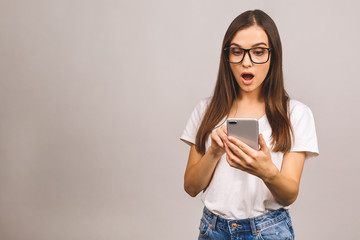 Fototapeta premium Portrait of a shocked amazed young girl using mobile phone isolated over grey background.