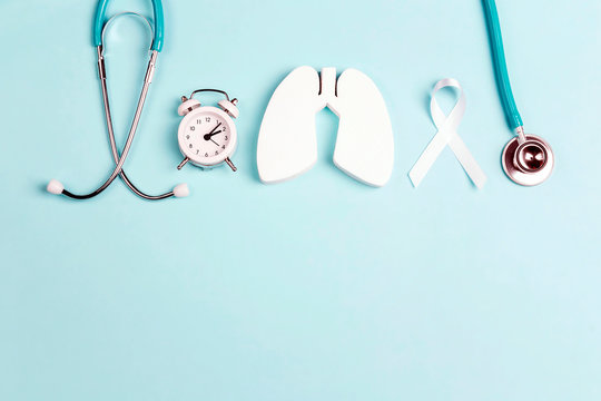 Lung cancer awareness background with white ribbon, alarm clock and stethoscope on blue.