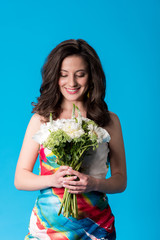 happy elegant young woman in dress holding flowers isolated on blue