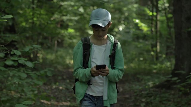 boy walking in the forest and uses a phone outdoors