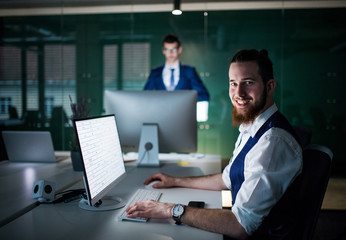 A portrait of young businessman with laptop sitting in an office.