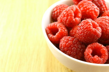 fresh red raspberry fruits in a small white bowl