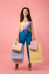 full length view of happy stylish disco girl holding shopping bags on pink