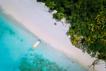 Top down aerial view of exotic tropical sandy beach with blue lagoon, palm trees and linely boat moored