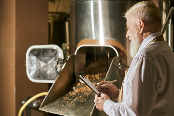Brewery expert monitoring milling process and writing.